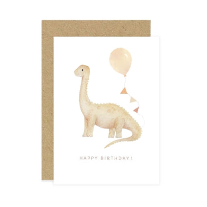 A children's birthday card with a kraft envelope, featuring a watercolor-style long-neck dinosaur holding a balloon and the words 'HAPPY BIRTHDAY!' on a white card.